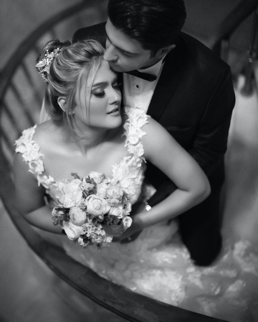 grayscale photo of woman in wedding dress holding bouquet of flowers